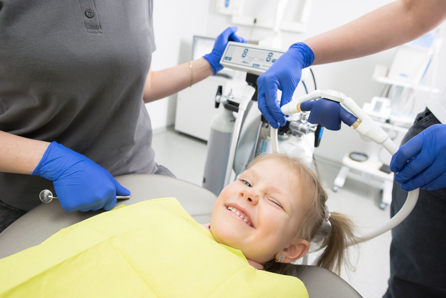 Cheerful child in a dental chair surrounded by pediatric dental staff