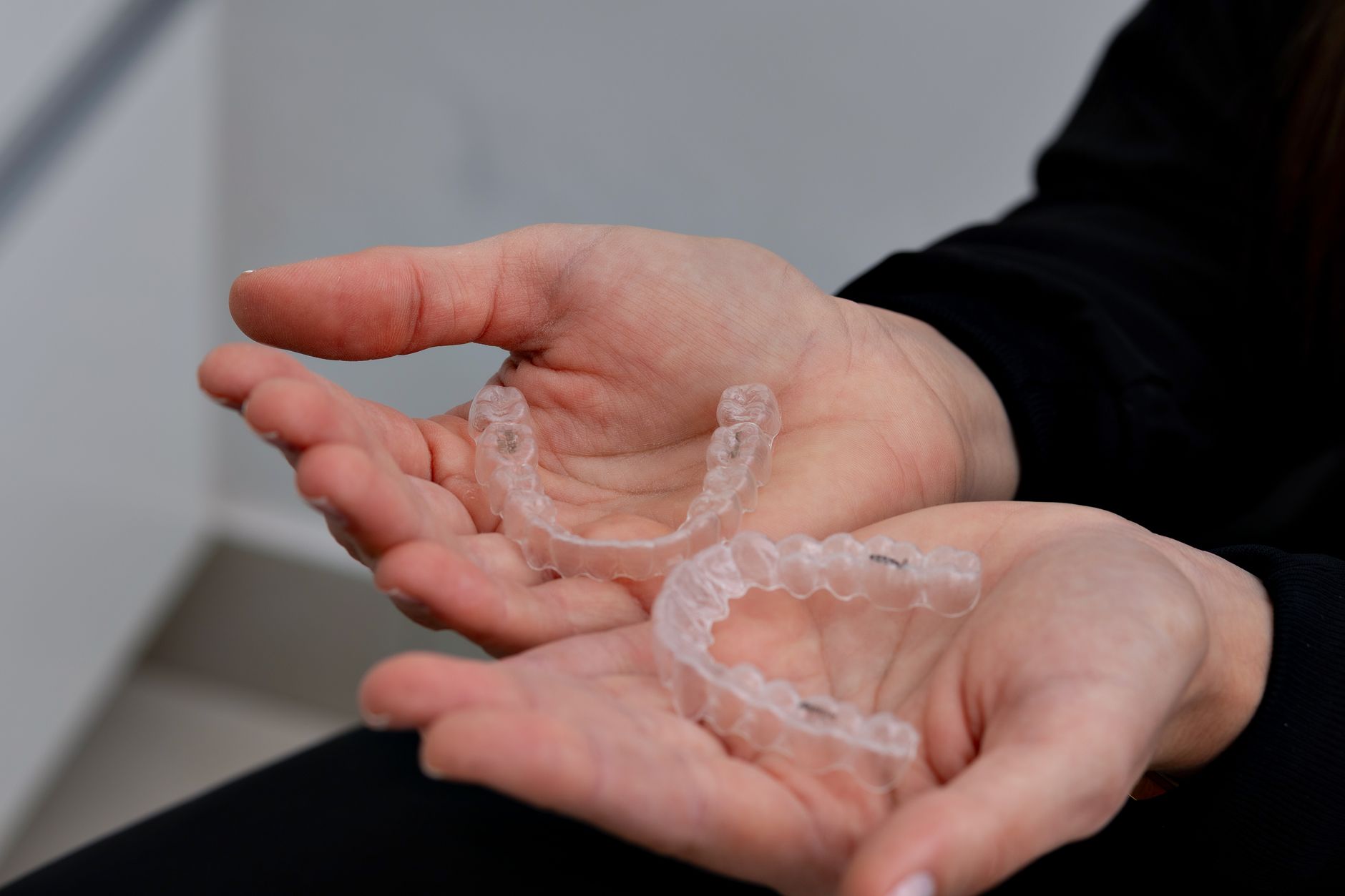 Hands holding clear plastic dental aligners in a dental office