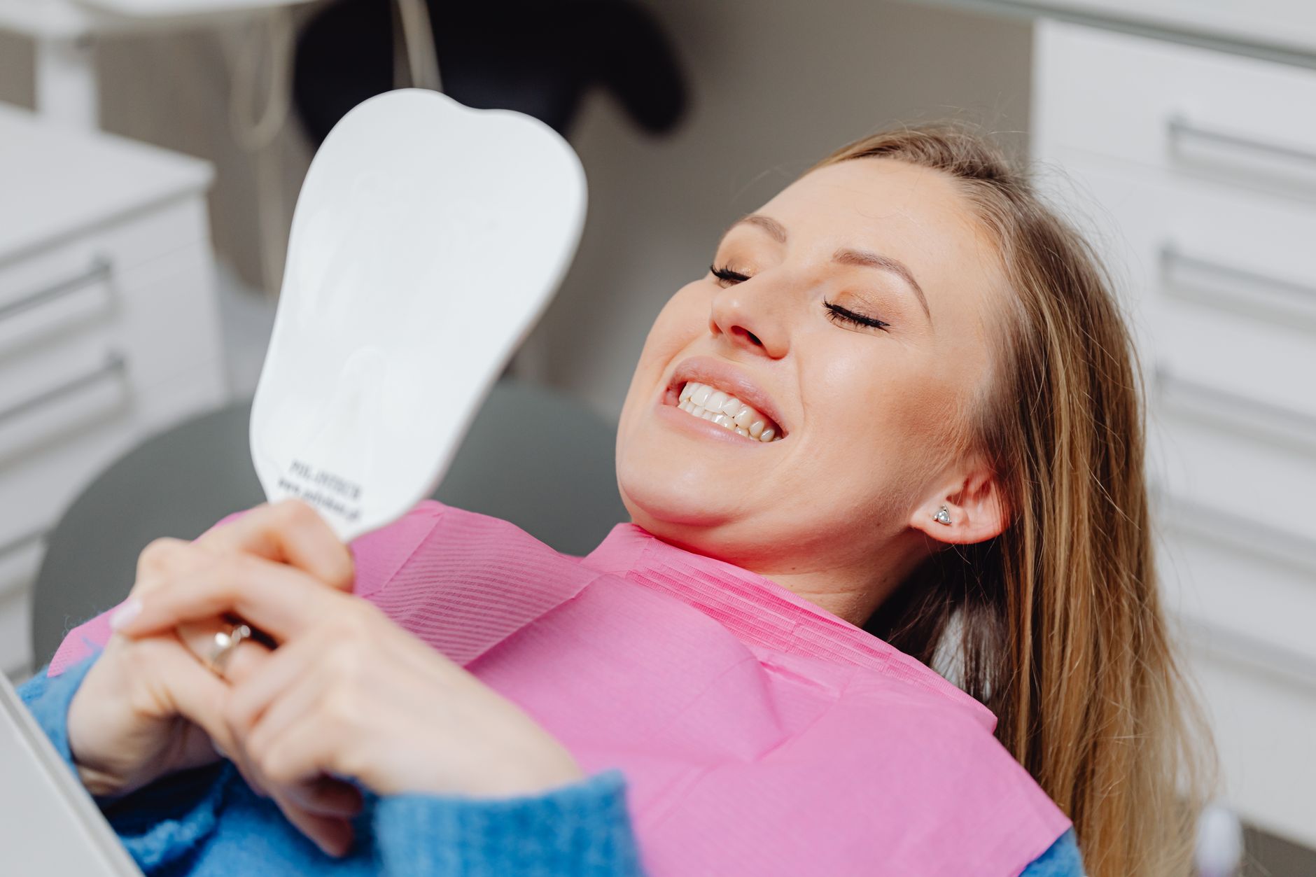 Woman smiling and checking her teeth in a hand mirror after a cosmetic dental visit