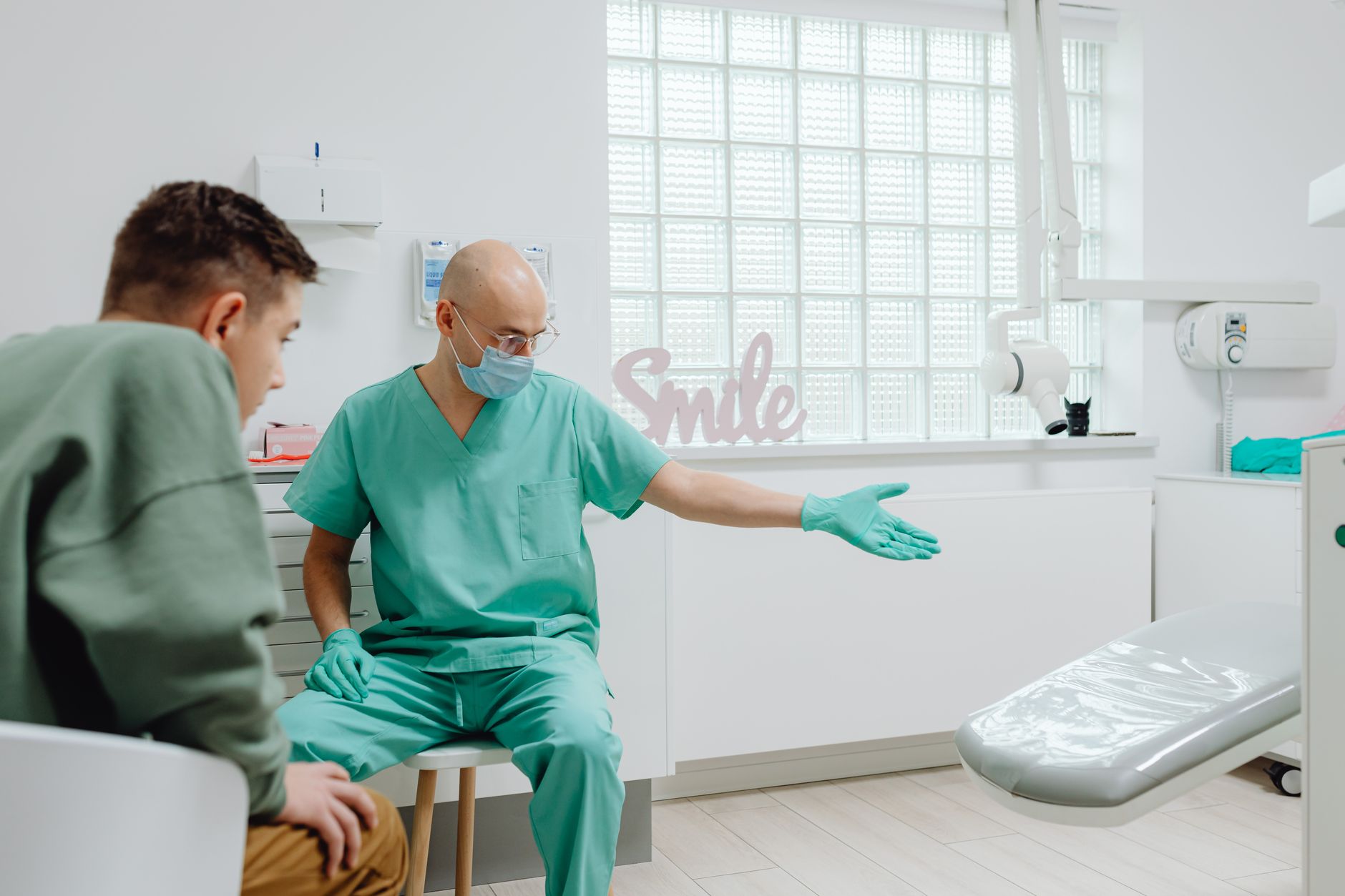 A dentist in scrubs talking to a patient in a bright modern clinic