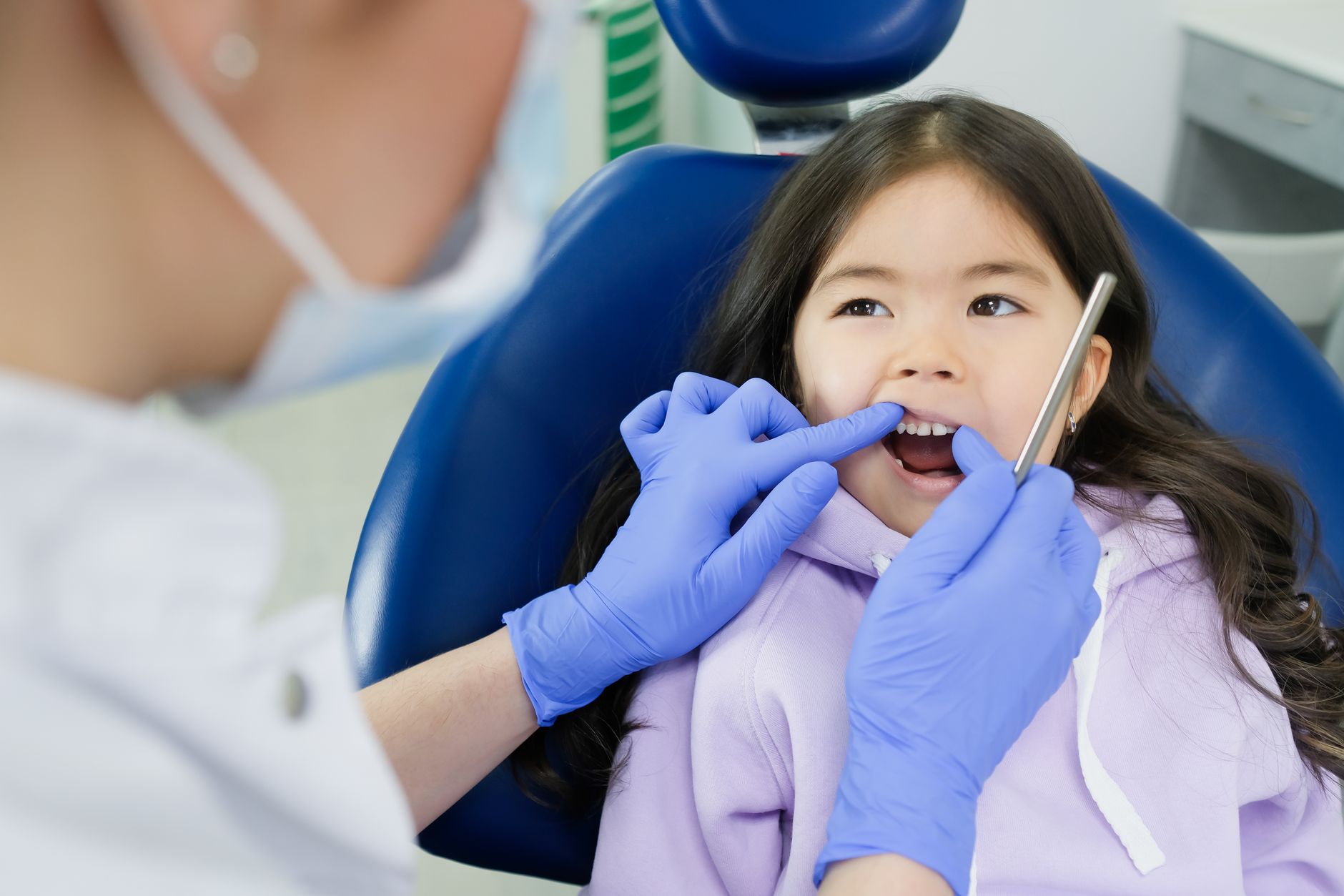 A young girl receives a dental checkup from a dentist wearing gloves